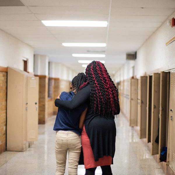 Teacher comforting a student as they walk down a school hallway.